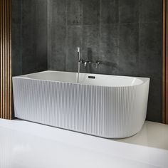 a large white bath tub sitting on top of a counter next to a wall mounted faucet