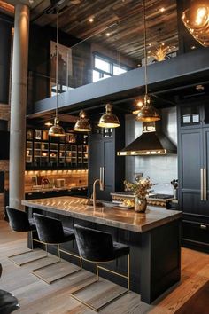 a large kitchen with black cabinets and gold accents on the countertop, along with two pendant lights hanging from the ceiling