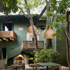 an outdoor dining area with wooden tables and chairs in front of a green building surrounded by trees