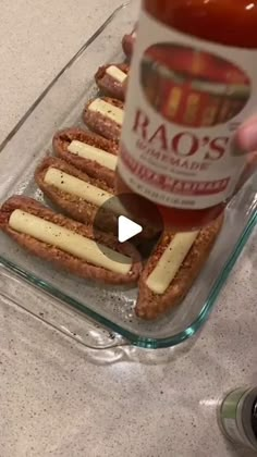 a person holding a bottle of ketchup and some hot dogs in a glass dish