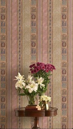 two vases with flowers on a table in front of a wallpapered background