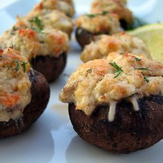 several stuffed mushrooms on a white plate with lemon wedges