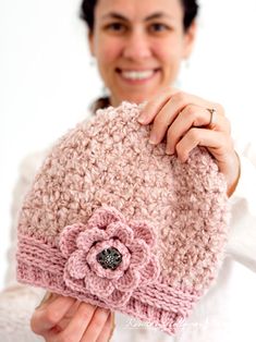 a woman holding up a pink crocheted hat with a flower on it's side