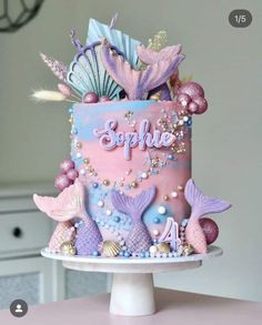 a pink and blue birthday cake with mermaid decorations on the top is decorated with seashells