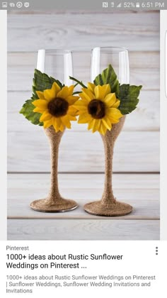 two wine glasses with sunflowers in them on top of a wooden table next to each other