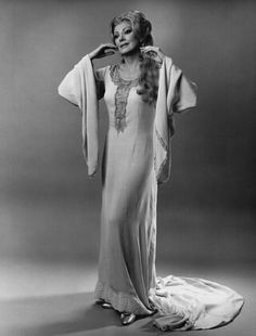 an old photo of a woman in a long white dress and coat with her hands on her head