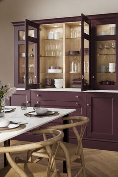 a dining room table with plates and glasses on it, in front of purple cabinets