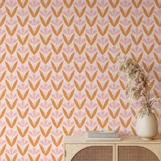 an orange and pink wallpaper with large leaves on the sideboard next to a white vase