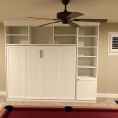 a pool table in front of a white bookcase with a ceiling fan above it