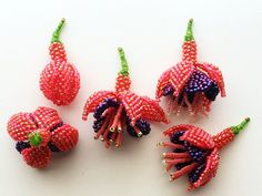 four beaded flowers are arranged on a white surface, one is pink and the other is green