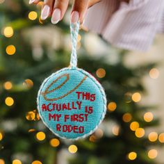 a hand holding a blue ornament that says, this actually is my first rodeo