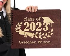 a woman holding up a wooden sign that says class of 202 with an image of a graduation cap on it