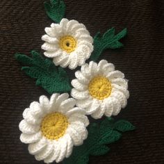 three crocheted white and yellow flowers sitting on top of a brown surface with green leaves