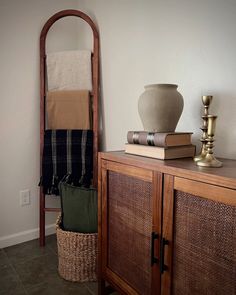 a wooden cabinet sitting next to a vase and some books on top of it in a room