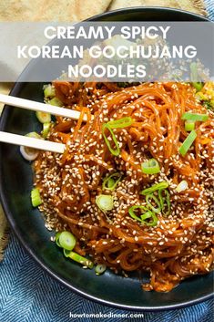 a black plate topped with noodles and vegetables next to chopsticks on a blue cloth