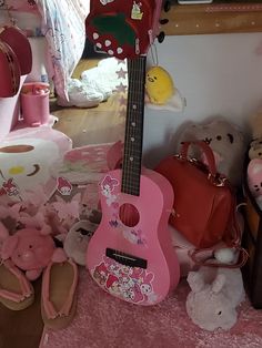 a pink guitar sitting on top of a bed next to stuffed animals and other toys