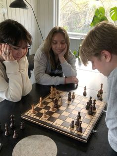 three people sitting at a table playing chess