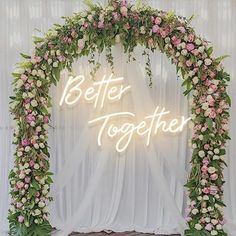 a neon sign that says better together with flowers and greenery on the wall behind it