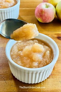 two small bowls filled with apple sauce on top of a wooden table next to apples