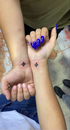 two people holding hands with tattoos on their fingers and wristbands, one has a cross tattoo on the other hand