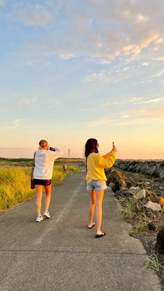 two people standing on the side of a road pointing at something in the sky above them