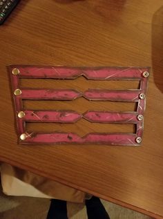 a wooden table topped with pink plastic and metal strips on it's sides, next to a remote control