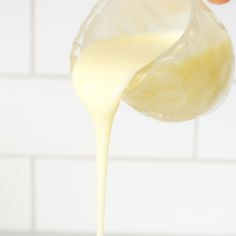 a person pouring milk into a bowl on top of a counter next to a white tile wall