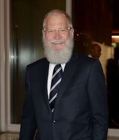 an older man in a suit and tie smiles for the camera while standing next to a doorway