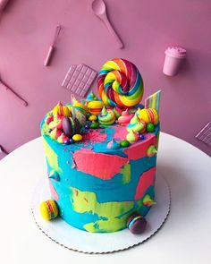 there is a colorful cake with candy on the top and pink wall in the background