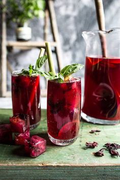 two glasses filled with red liquid and garnished with green leafy leaves, sitting on a wooden table