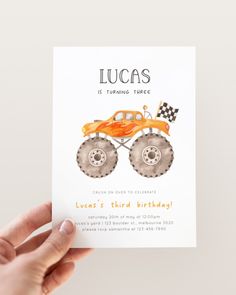 a hand holding up a birthday card with an orange monster truck on it's front