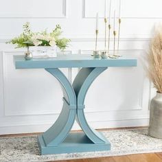 a blue table sitting on top of a wooden floor next to a vase filled with flowers