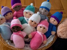 a basket filled with knitted dolls sitting on top of a wooden floor next to balls of yarn