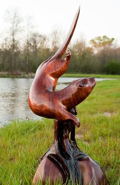 a wooden sculpture of two birds on top of each other in the grass next to a body of water