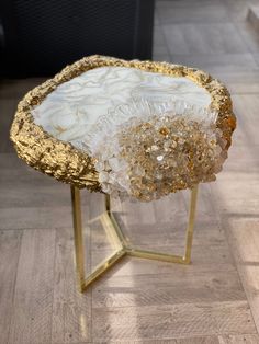 a gold and white table with some glass beads on it's legs, sitting on a wood floor