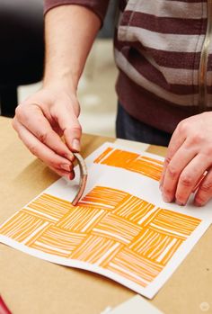 a person is cutting paper with scissors on top of a cardboard box that has an orange and white pattern