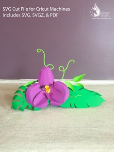 a paper flower sitting on top of a wooden table next to a purple wall and green leaves