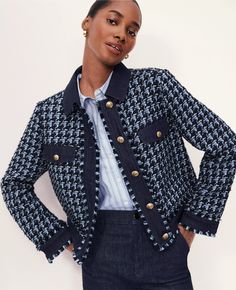 a woman wearing a jacket and jeans standing in front of a white wall with her hands on her hips