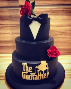 a three tiered black cake with red roses on top and the godfather logo