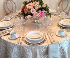 the table is set with white plates and silverware, pink flowers are in vases