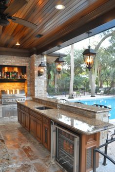 an outdoor kitchen with granite counter tops and stainless steel appliances, along with a pool in the background