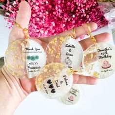 four personalized key chains in the palm of someone's hand with flowers behind them