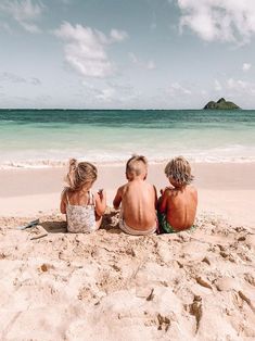 three children sitting on the beach looking out at the ocean