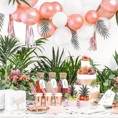 a table topped with lots of pink and white balloons next to greenery covered walls