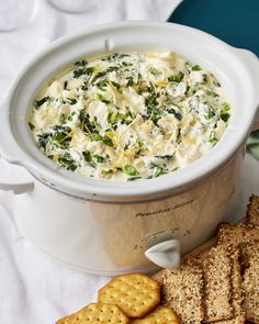 a crock pot filled with spinach and cheese next to crackers on a table