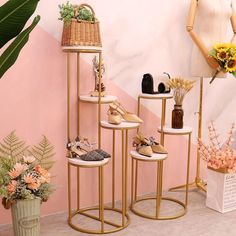 three tiered display stands with shoes and flowers in front of a pink painted wall