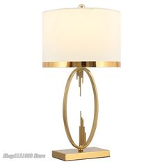 a table lamp with a white shade on top and a gold base, sitting on a white background