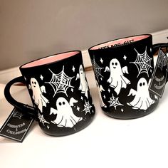 two coffee mugs decorated with black and white ghost images, one has pink rim