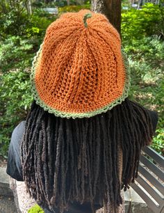 a person with dreadlocks sitting on a bench wearing an orange knitted hat