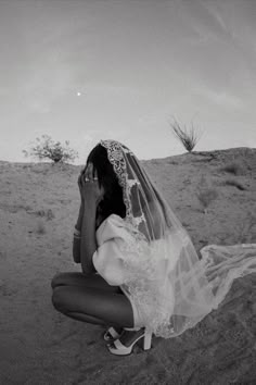 a woman kneeling in the sand with her veil over her face and hands to her face